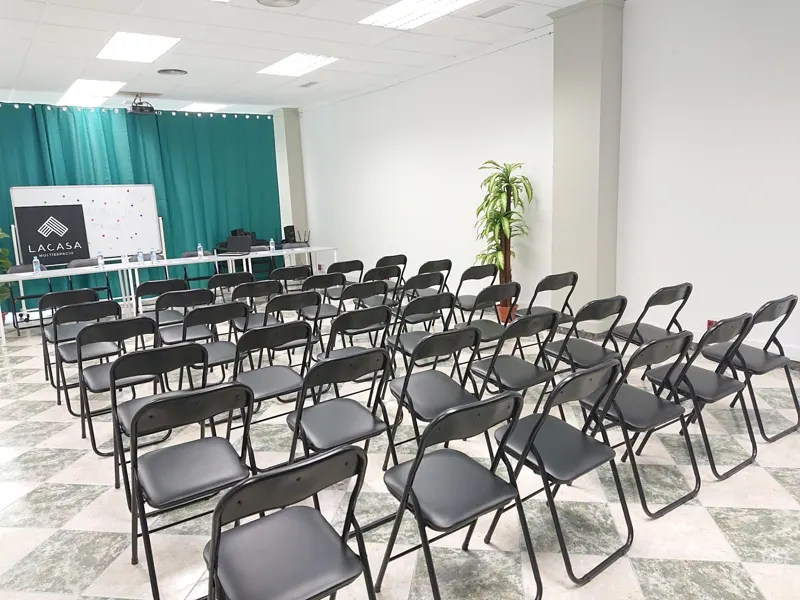 Sala de Lacasa montada como auditorio, con filas de sillas negras frente a la pantalla y las cortinas verdes