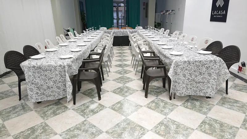 Dos mesas largas con mantel estampado y sillas negras preparadas para una comida