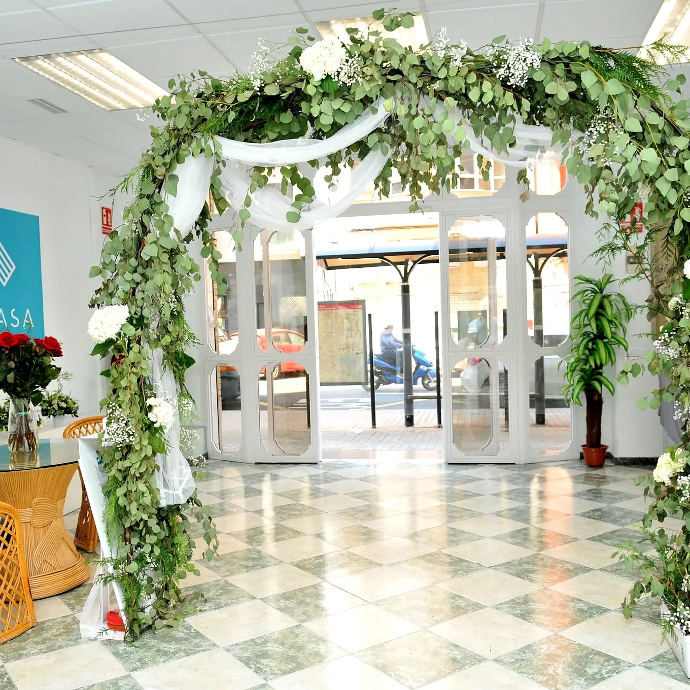 Arco de flores blancas y verdes en la entrada de la sala para una comunión