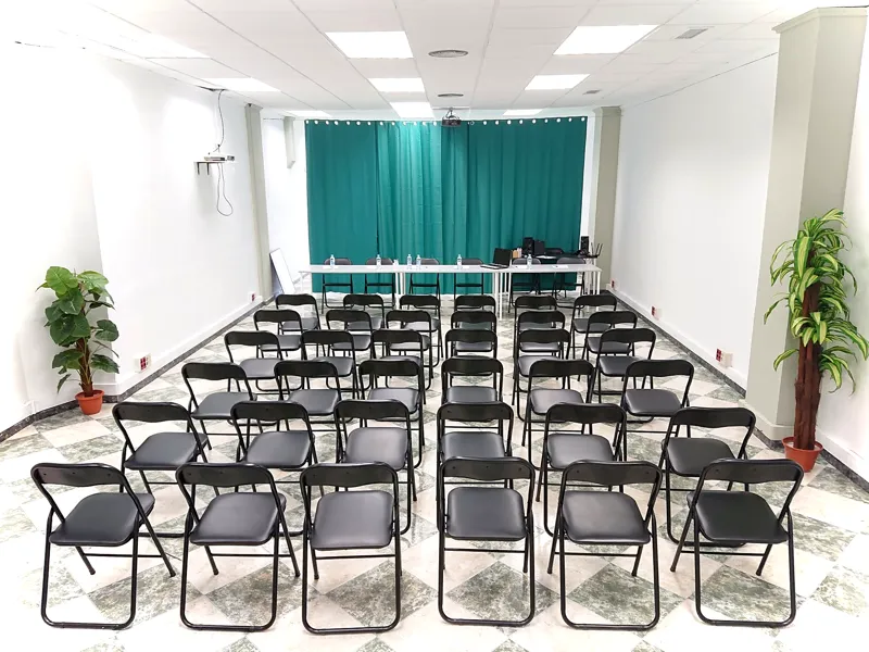 Sala montada como auditorio con sillas negras en filas frente a las cortinas verdes