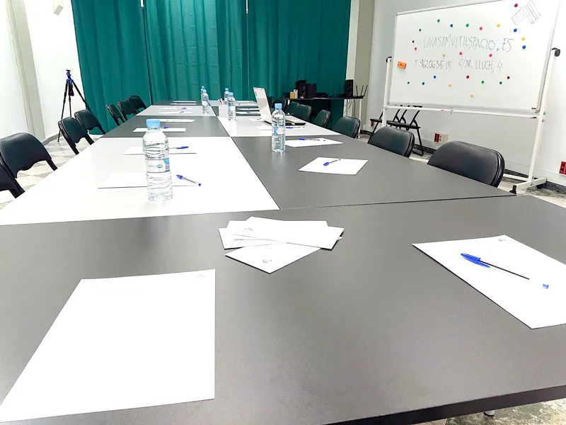Mesas de reunión con folios, agua y una pizarra al fondo