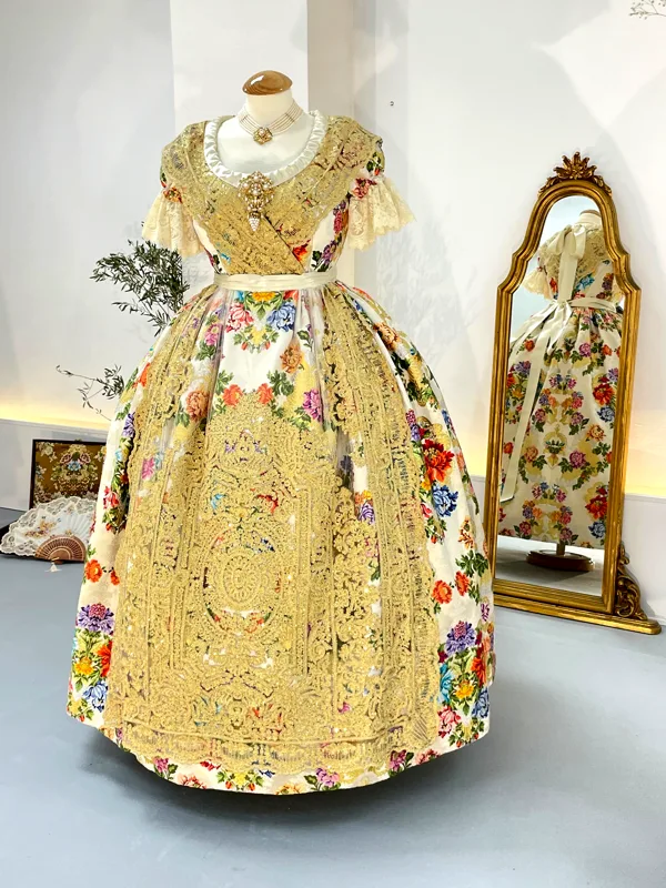 Traje de fallera de espolín con flores bordadas junto a un espejo dorado