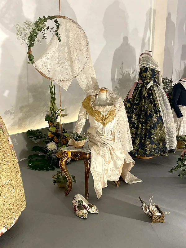 Exposición de trajes de fallera con aros de flores y ramos en el suelo